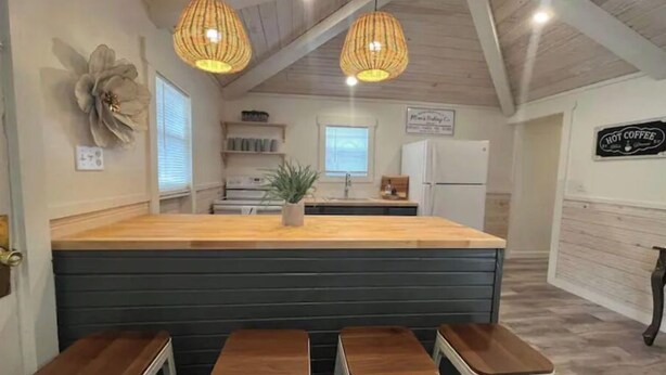 A kitchen with a central island, bar stools, pendant lights, and a refrigerator. - River Rock Cabin - Near Spring River and Main St (Mammoth Spring)