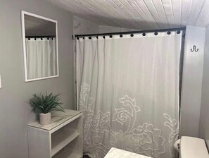 A bathroom with a shower curtain, a mirror, a potted plant, and a toilet.