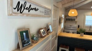 A kitchen area with a 'Welcome to our HOME' sign, a wooden shelf with framed photos, and a hanging pendant light. - River Rock Cabin - Near Spring River and Main St (Mammoth Spring)