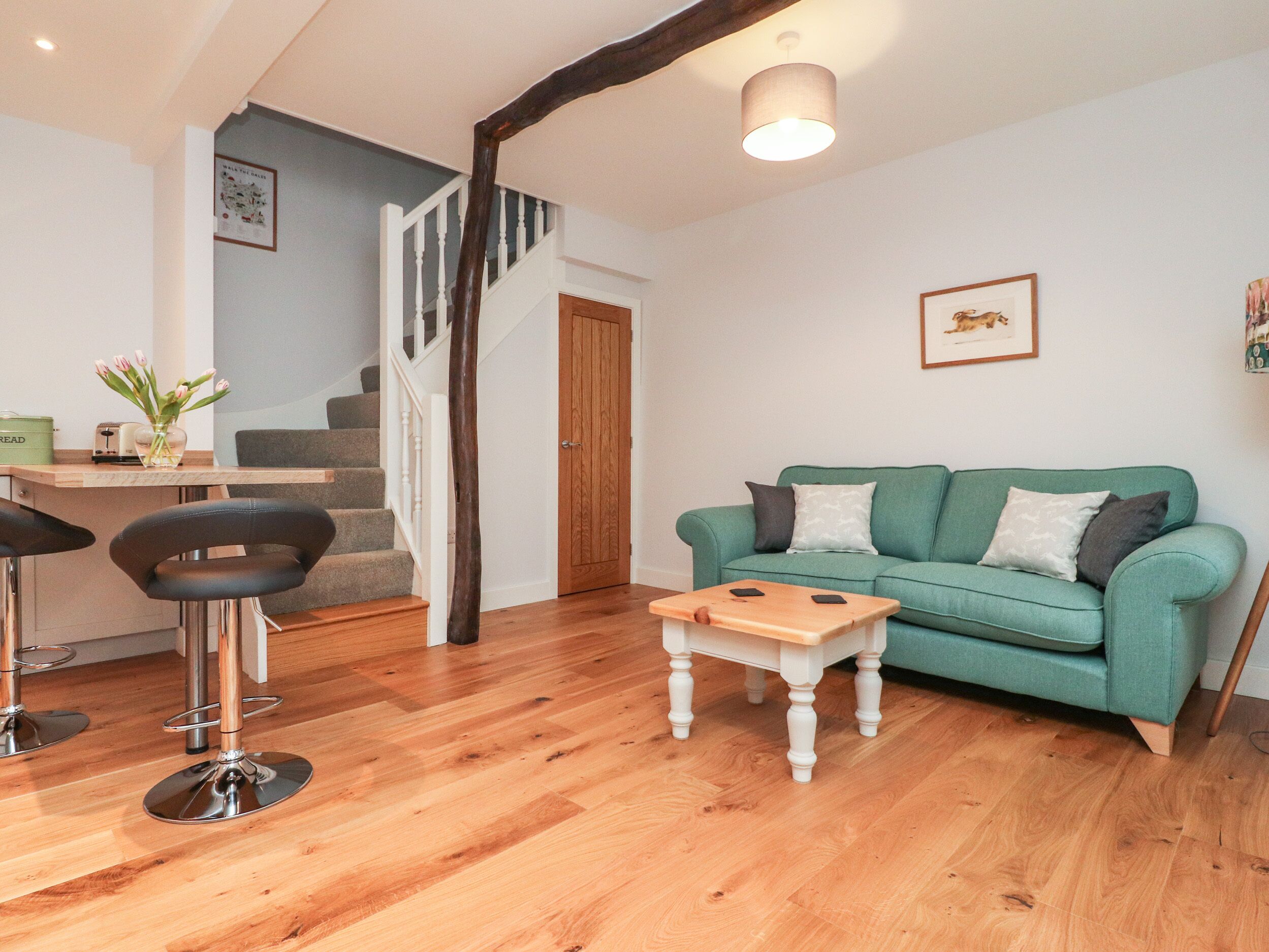 A modern living room with a teal sofa, a wooden coffee table, and a staircase leading to another floor.