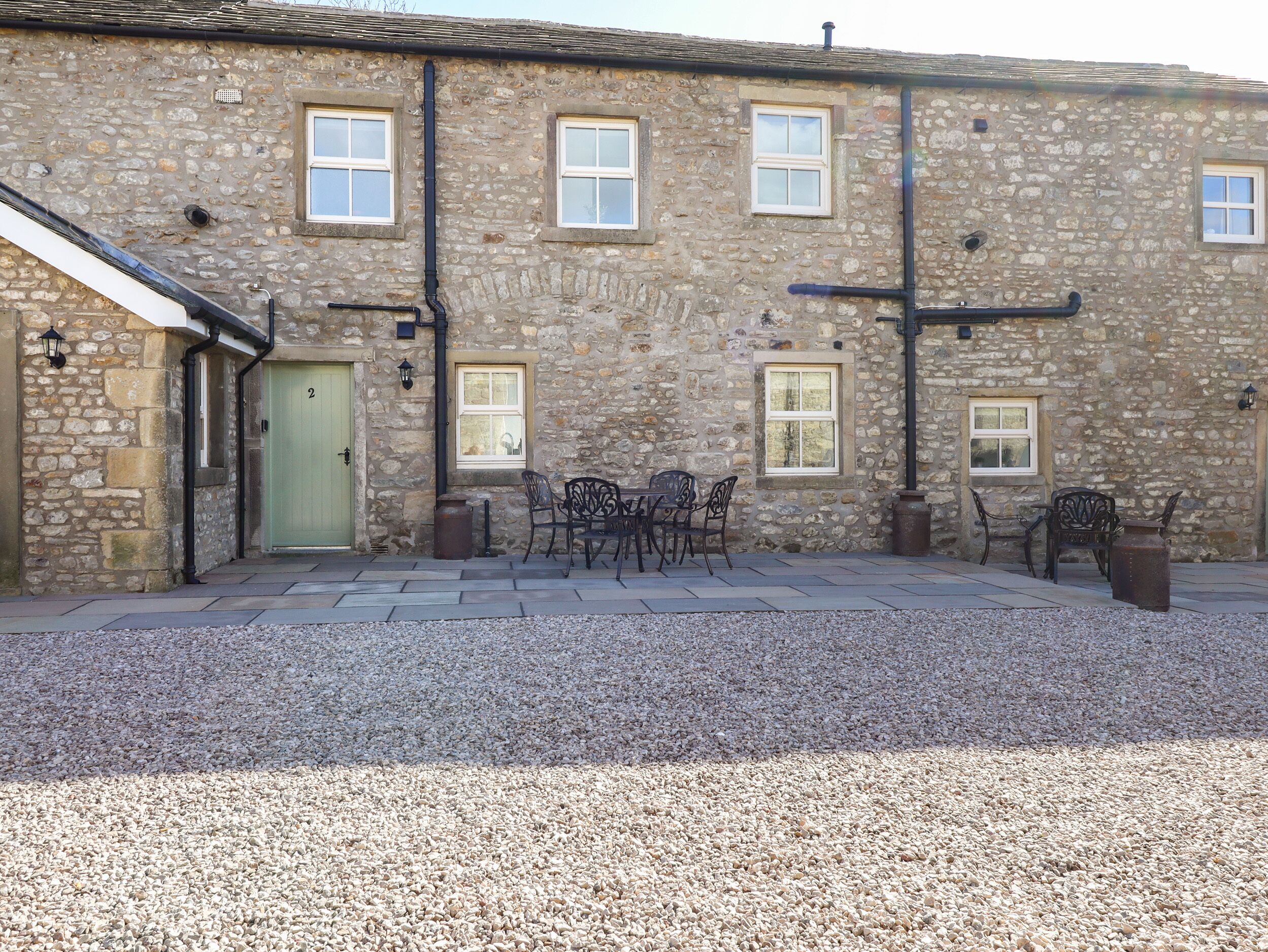 A stone building with a green door, multiple windows, outdoor seating, and a gravel courtyard.