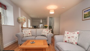 A living room with a grey sofa set, a wooden coffee table, and a kitchen in the background. - 1 Hull House Cottage (Skipton)
