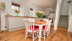 A modern kitchen with white cabinetry, a wooden dining table, and four white chairs with red cushions. - 1 Hull House Cottage (Skipton)