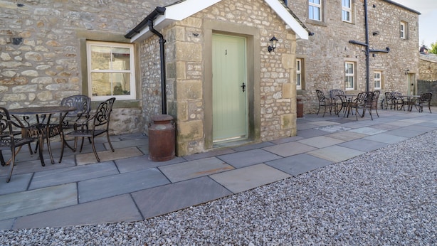 A stone building with a green door, outdoor seating area with metal chairs, and a gravel path. - 1 Hull House Cottage (Skipton)