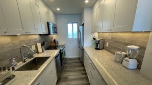 Una cocina moderna con armarios blancos, un refrigerador de acero inoxidable, una cafetera y una licuadora.