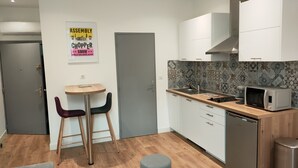 A compact kitchen with white cabinets, a microwave, and a sink. There's a small round table with two chairs and a poster on the wall. - Charming studio downtown Ajaccio (Ajaccio)