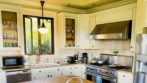 A modern kitchen with a central island, stainless steel appliances, and white cabinetry. - Walk to Poipu Beach • 4BR + Bonus • Pool (Koloa)