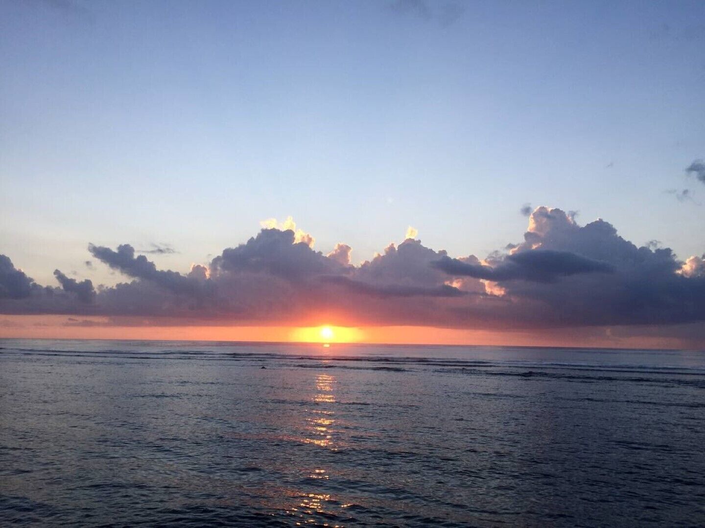 Un coucher de soleil sur une mer calme, avec des nuages dans le ciel.