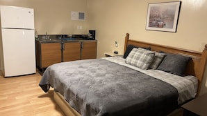 Ein kleines Hotelzimmer mit Bett, einer kompakten Küchenzeile, einem Kühlschrank und einem gerahmten Bild an der Wand.