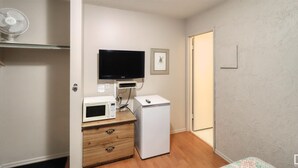 Ein gemütlicher Raum mit einem an der Wand befestigten Flachbildfernseher, einer Mikrowelle, einem Minikühlschrank und einer Holzkommode mit Schubladen.