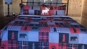 Un dormitorio acogedor con techo de madera, una cama con colcha de estampados de animales, una lámpara y un cuadro colgado en la pared de un alce.