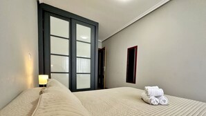Una habitación de hotel con una cama grande, una mesita de noche con lámpara y una ventana con persianas.