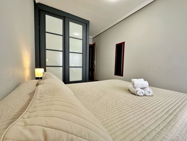 A hotel room with a large bed, a nightstand with a lamp, and a window with blinds. - Apto céntrico con garaje - Abad Paterno 3008 (Santoña)