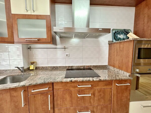 Una cocina con armarios de madera, una campana extractora de acero inoxidable, un horno empotrado y encimera de granito.