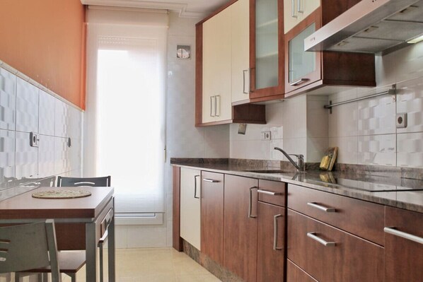 A kitchen with wooden cabinets, a marble countertop, and a window with a view. - Apto céntrico con garaje - Abad Paterno 3008 (Santoña)