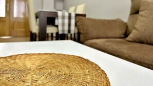 Una sala de estar con una mesa blanca, un sofá marrón y un comedor con mantel a cuadros.