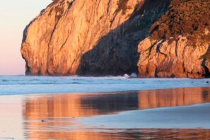 Una gran formación rocosa junto al mar, con una playa arenosa al frente.