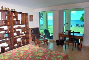 A room with a bed, a desk, a chair, a bookshelf, and a view of the ocean.
