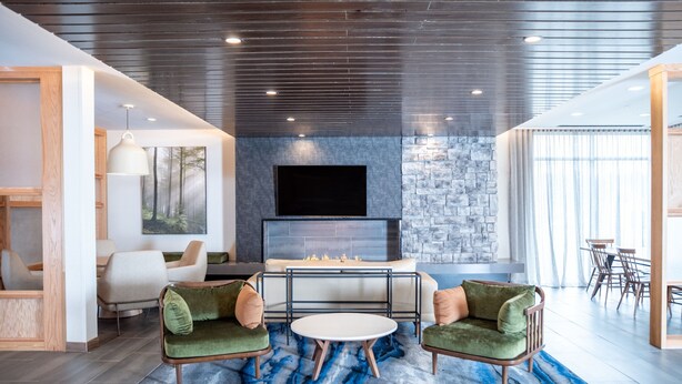 A modern living room with a fireplace, green armchairs, a round coffee table, and a stone accent wall. - Fairfield Inn & Suites by Marriott Kingsport (Kingsport)