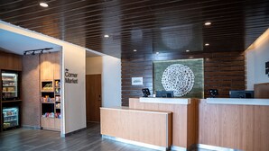 A reception area with a wooden reception desk, a sign for 'The Corner Market', and a decorative wall piece. - Fairfield Inn & Suites by Marriott Kingsport (Kingsport)
