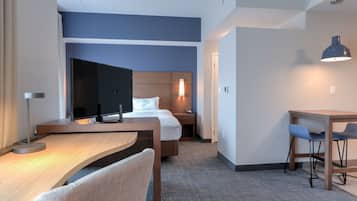 Una habitación de hotel con cama, escritorio, silla, televisor, lámpara y una pequeña mesa con sillas.