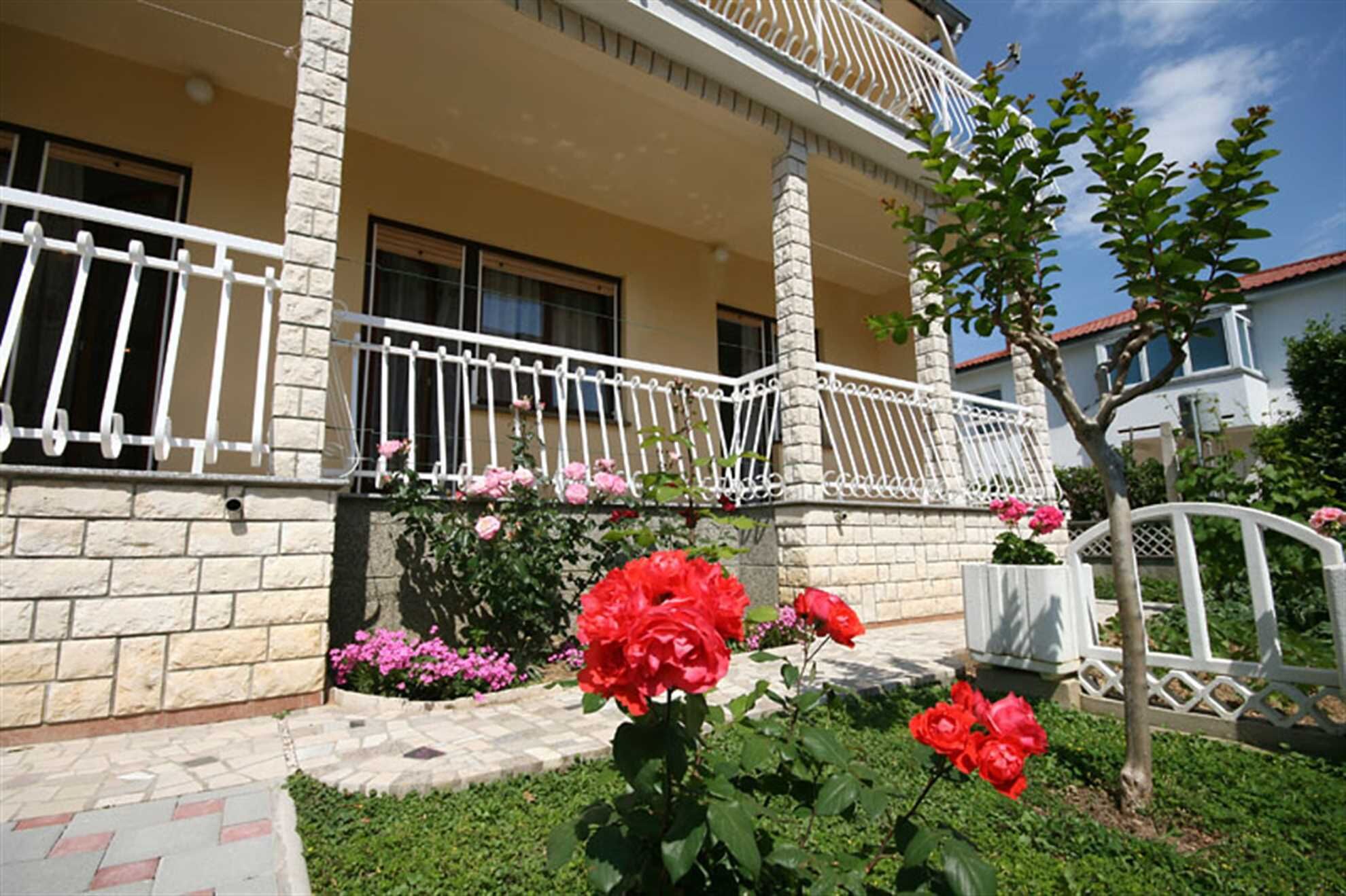 A two-story building with a balcony, stone facade, and a garden with red roses.