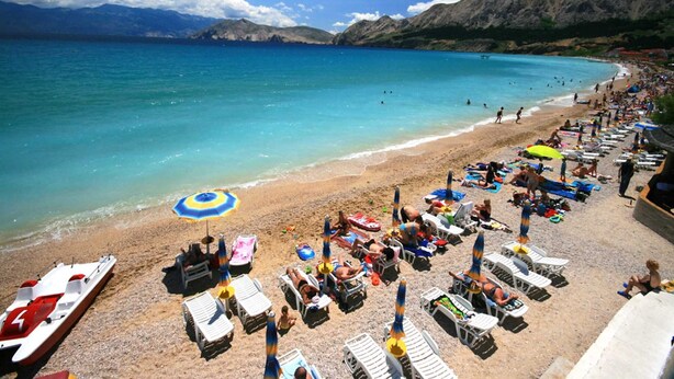 A beach with sun loungers and umbrellas, a boat, and mountains in the background. - Anica  A4 -  Apartment with two bedrooms (Baška)