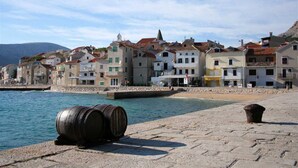 A coastal town with buildings along the waterfront, a stone-paved promenade, and barrels on the shore. - Anica  A4 -  Apartment with two bedrooms (Baška)