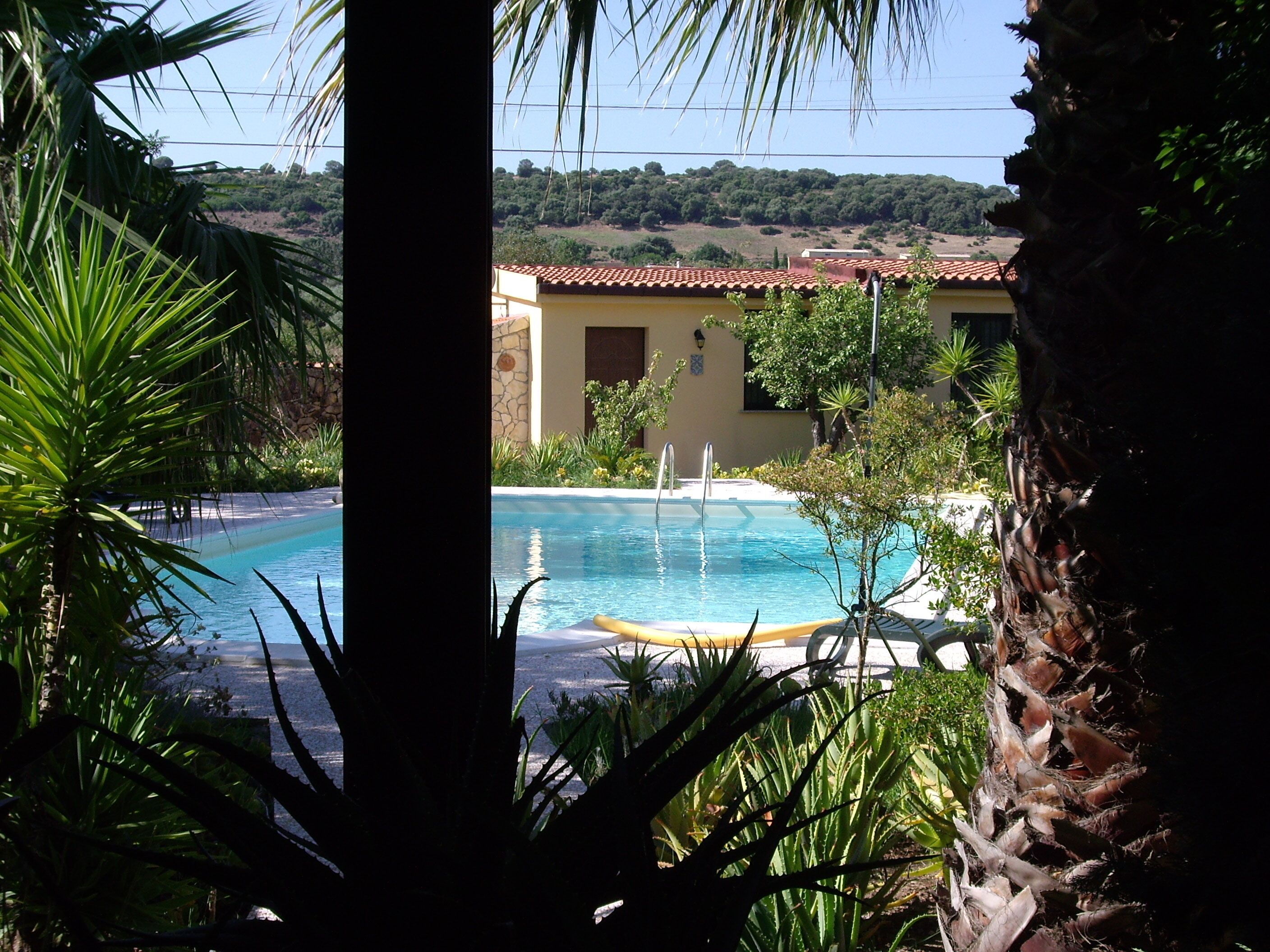 Zona de piscina con vista despejada a un edificio de techo con tejas y pared de piedra.