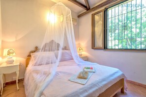 A bedroom with a canopy bed, bedside lamps, a window with bars, and a view of greenery. - Cottage Soraya with independent swimming pool near Alghero and the beach (Sardegna)