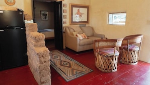 A living room with a black refrigerator, a stone pillar, a beige sofa, two wicker chairs, and a patterned rug.