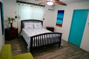 A bedroom with a wooden bed, a nightstand, a lamp, a potted plant, and a door.