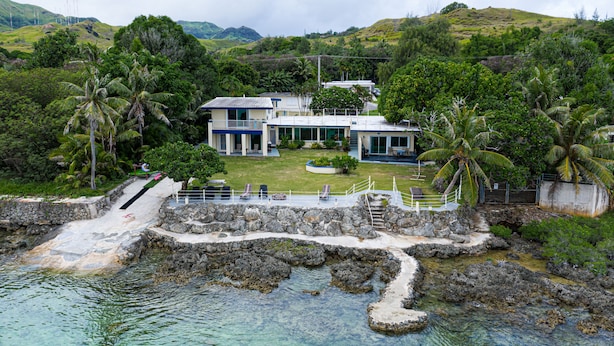 Une propriété située sur la côte, dotée d’une zone de baignade bien délimitée, d’un chemin de pierre menant à un bâtiment et d’une végétation luxuriante.