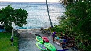 Un chemin en béton qui mène à une plage où se trouvent plusieurs kayaks et une planche à pagaie.