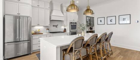 Una cocina moderna con armarios blancos, electrodomésticos de acero inoxidable y una isla central con taburetes de bar.