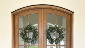 Una puerta doble de madera con paneles de vidrio y dos coronas decorativas.