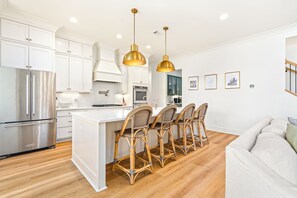 A modern kitchen with white cabinetry, stainless steel appliances, and a central island with wicker chairs.