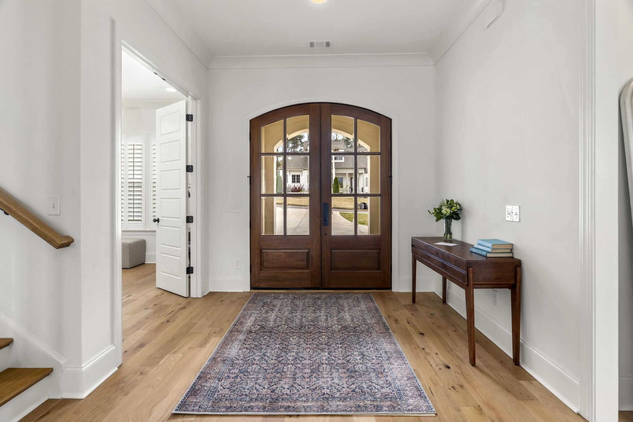 A hallway with a wooden floor, a patterned rug, a wooden bench, and a door with glass panels.