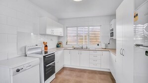 A compact kitchen with white cabinetry, a built-in oven, a dishwasher, and a window with blinds. - 13 Indigo Avenue - 'Indigo Sands' - Rainbow Beach. Beds made for arrival. Close to beach (Rainbow Beach)