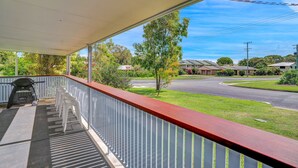 A covered balcony with a grill and white plastic chairs, overlooking a residential street with houses and greenery. - 13 Indigo Avenue - 'Indigo Sands' - Rainbow Beach. Beds made for arrival. Close to beach (Rainbow Beach)