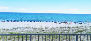 Une plage bordée de rangées de parasols bleus et de chaises longues, un rivage sablonneux et l’océan en toile de fond.