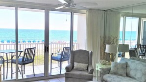 A living room with a view of the ocean, a sofa, a chair, a table, and a TV.