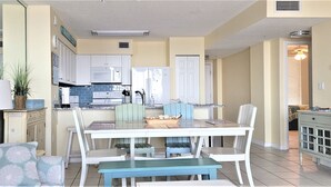 A compact kitchen with white cabinets, a microwave, and a stove. There is a dining area with a table and chairs, and a small seating area with a couch and pillows.