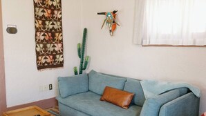 Un salon avec un canapé bleu clair, un coussin marron, un cactus, une décoration murale et une petite table en bois sur laquelle se trouve une télécommande.