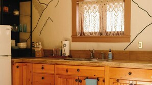 Une cuisine avec des meubles de rangement en bois, un réfrigérateur, un évier et une fenêtre ornée de rideaux en dentelle.
