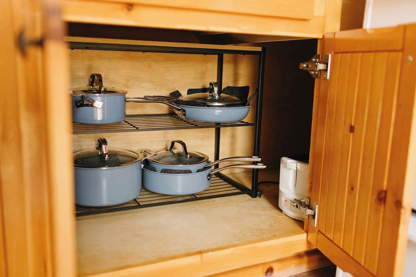 A kitchen cabinet with three shelves, each holding a pot with a lid.
