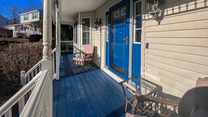 A porch with a blue door, a wicker chair, and a glass table.