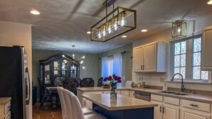 A kitchen with white cabinets, a blue island, and a chandelier.