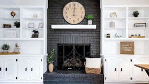 A living room with a fireplace, white shelving units, and a clock above the mantel. - Heated Pool-HotTub-Game Room-Fire Pit-Big Backyard (San Antonio)