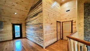 A spacious room with wooden walls and a wooden floor, featuring a staircase with a wooden railing and a door with a window. - Luxury Mtn View Cabin w/ Theater, Hot Tub, Game Room, EV Charger, Sleeps 12 (Gatlinburg)